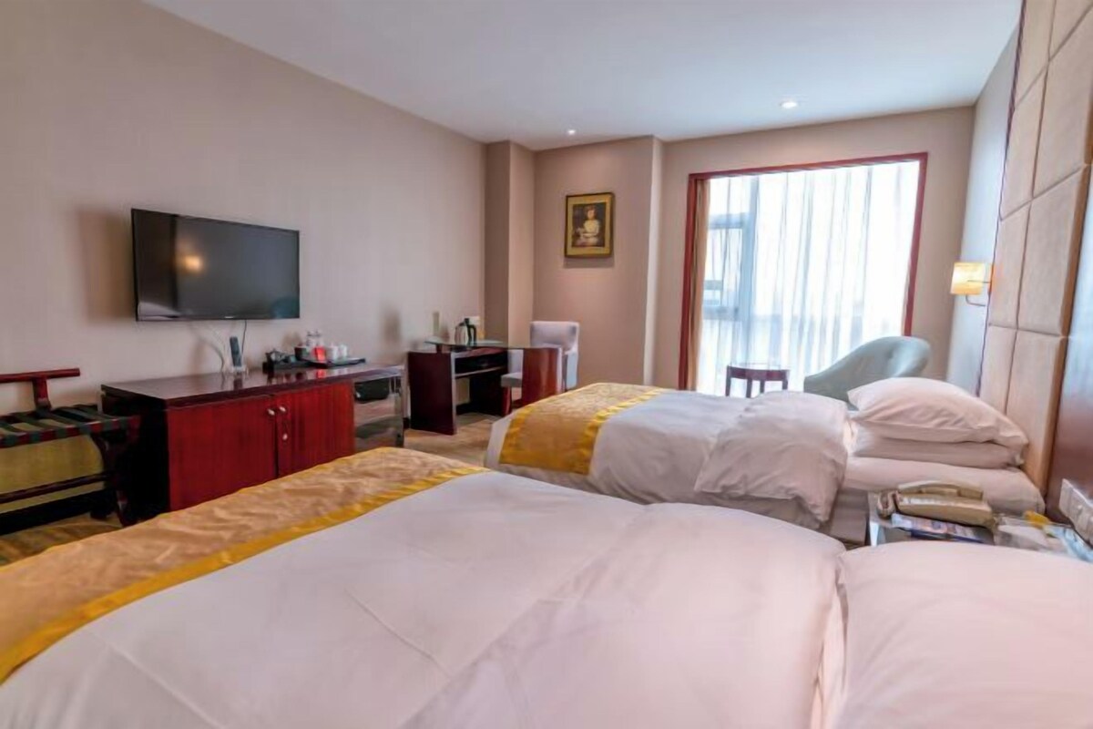 Une chambre d’hôtel avec deux lits, une télévision, un bureau, une chaise et une fenêtre avec des rideaux.