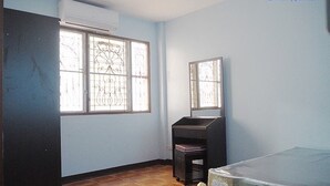 A room with a bed, a desk, and a window with metal bars. - The Trust Guesthouse (Pak Kret)