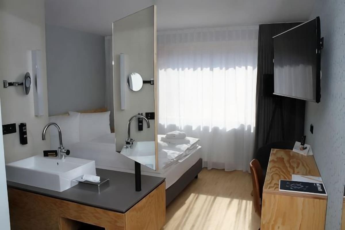 Ett modernt hotellrum med dubbelt handfat, en stor spegel, en platt-TV och ett skrivbord i trä.