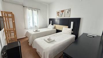 Habitación de hotel con dos camas, un escritorio, una silla, aire acondicionado y una ventana con cortinas.