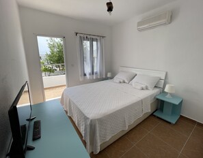 A bedroom with a bed, a nightstand, a lamp, a TV, and a window with curtains. - Esmana Otel (Bodrum)