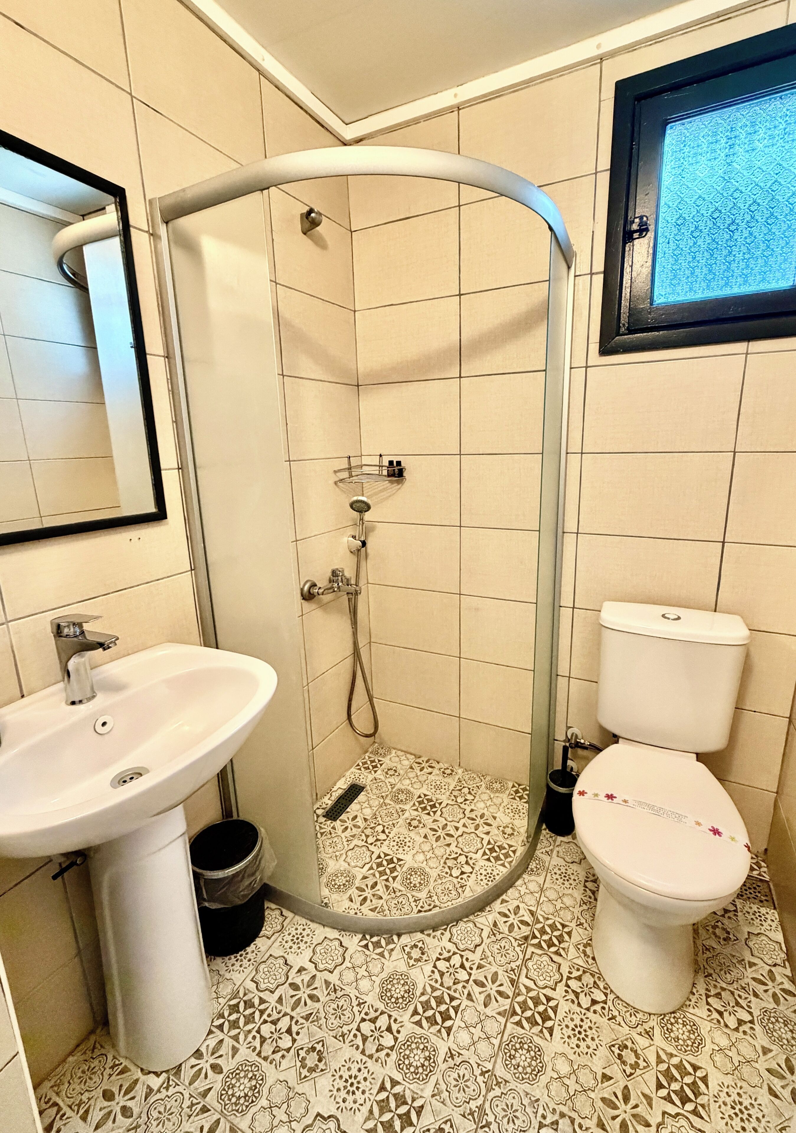 A bathroom with a shower, sink, toilet, and patterned floor tiles.