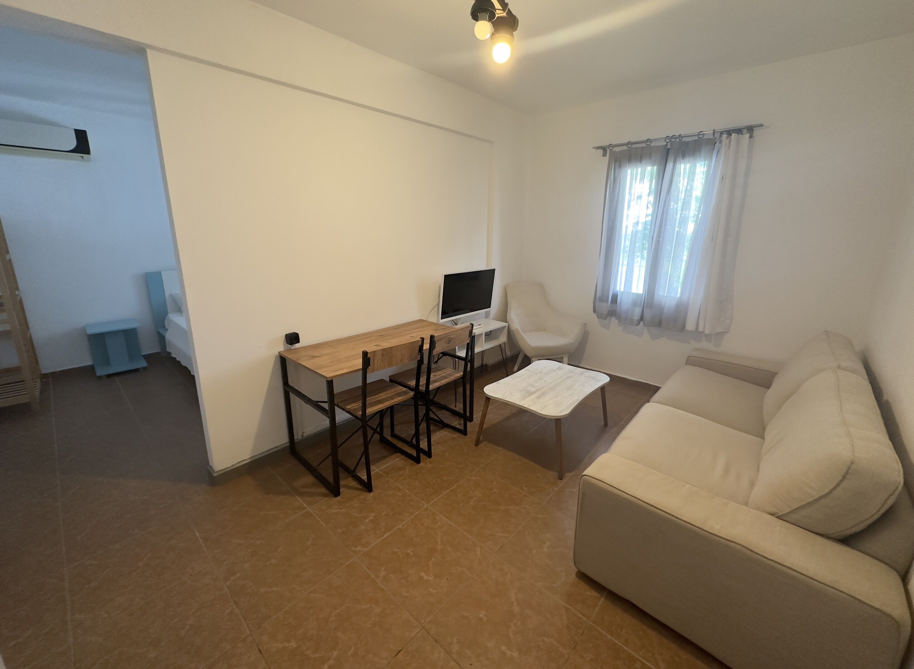 A living room with a wooden dining table, a sofa, a TV, and a window with curtains.