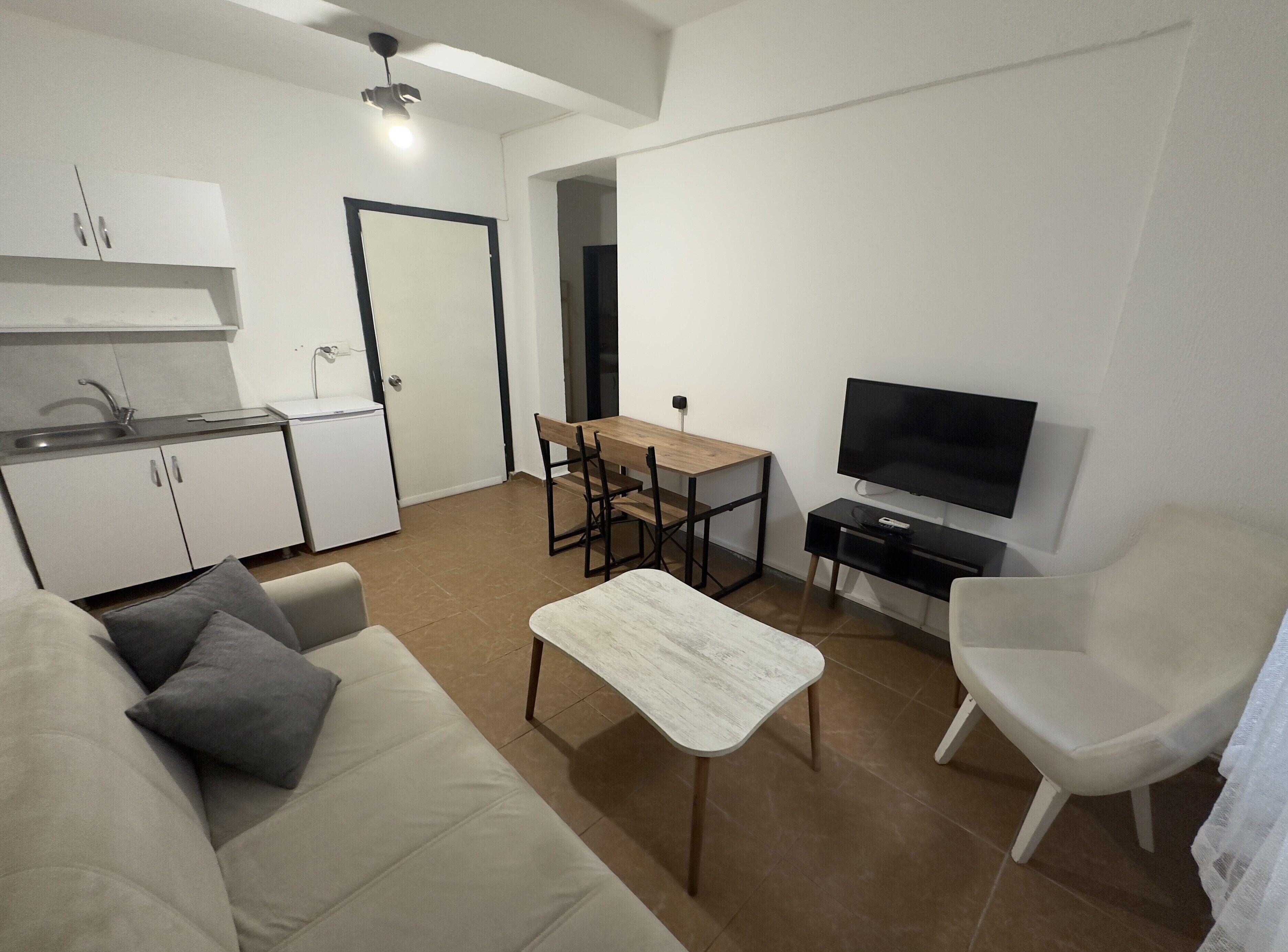 A modern living room with a sofa, a coffee table, a TV, and a dining area with a table and chairs.