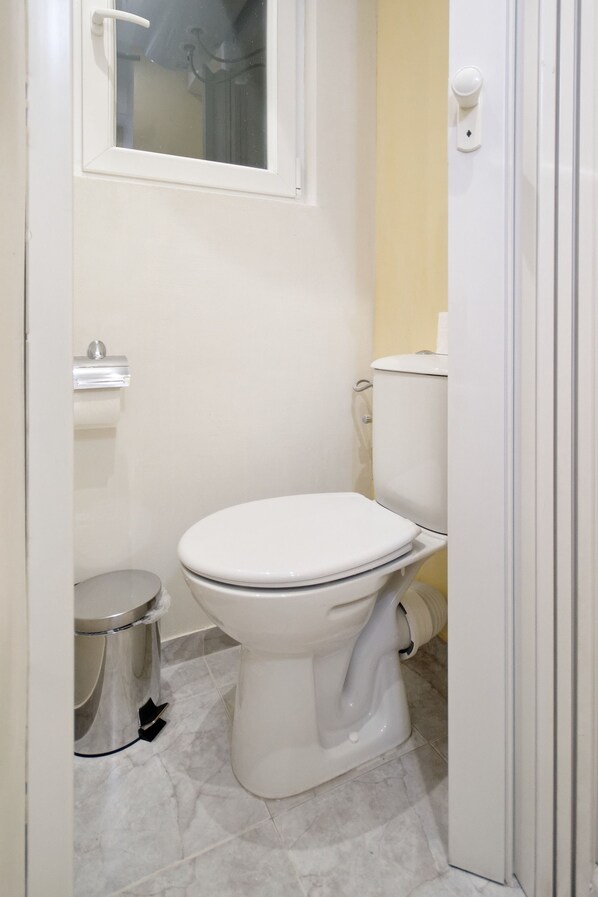 Une petite salle de bain propre, avec des toilettes blanches, une poubelle et un porte-rouleau de papier toilette.