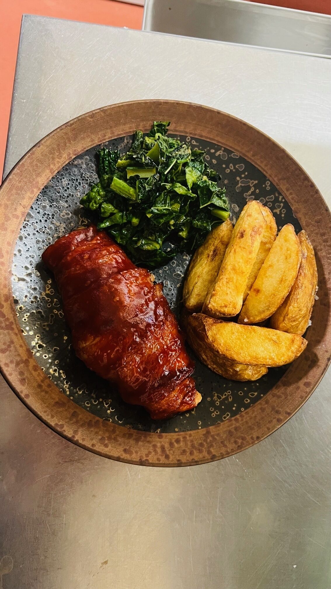 A plate with a meat dish, roasted potatoes, and sautéed greens.