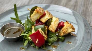 A plate of food with grilled chicken, greens, and a small bowl of sauce.