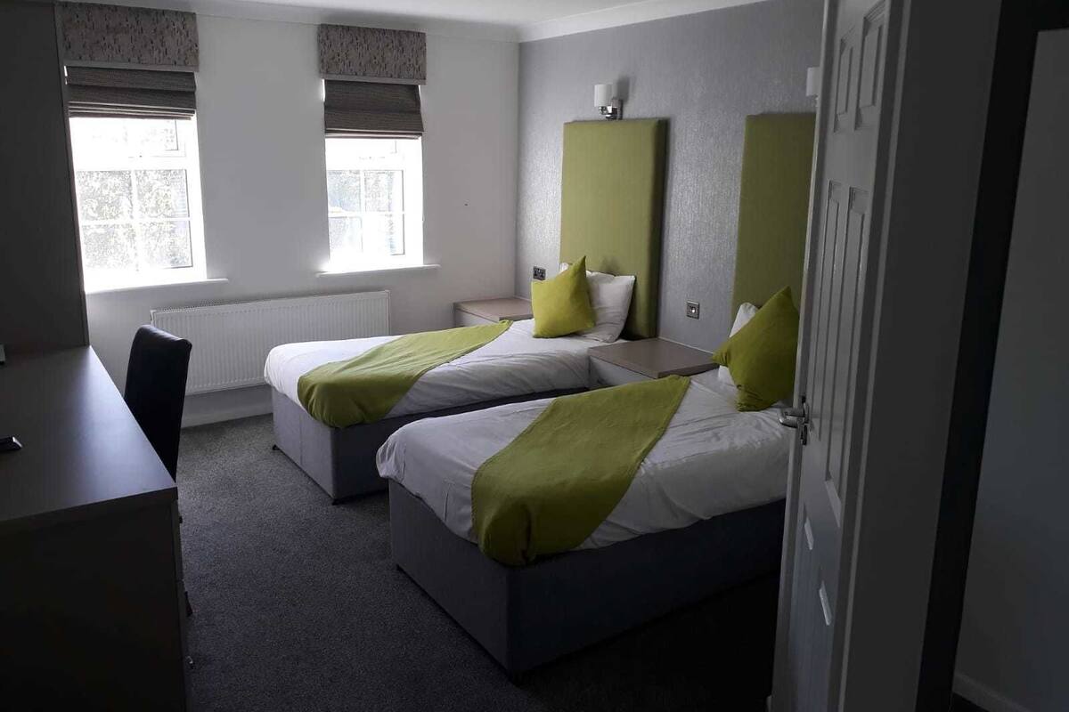 A hotel room with two beds, a desk, and a radiator.