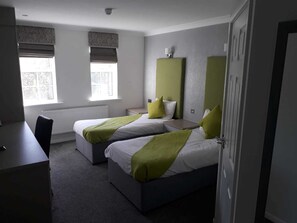 A hotel room with two beds, a desk, and a radiator.