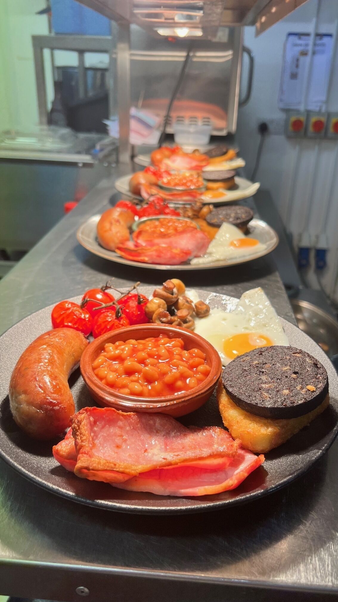 A breakfast buffet with various dishes including eggs, sausages, beans, tomatoes, and bacon.