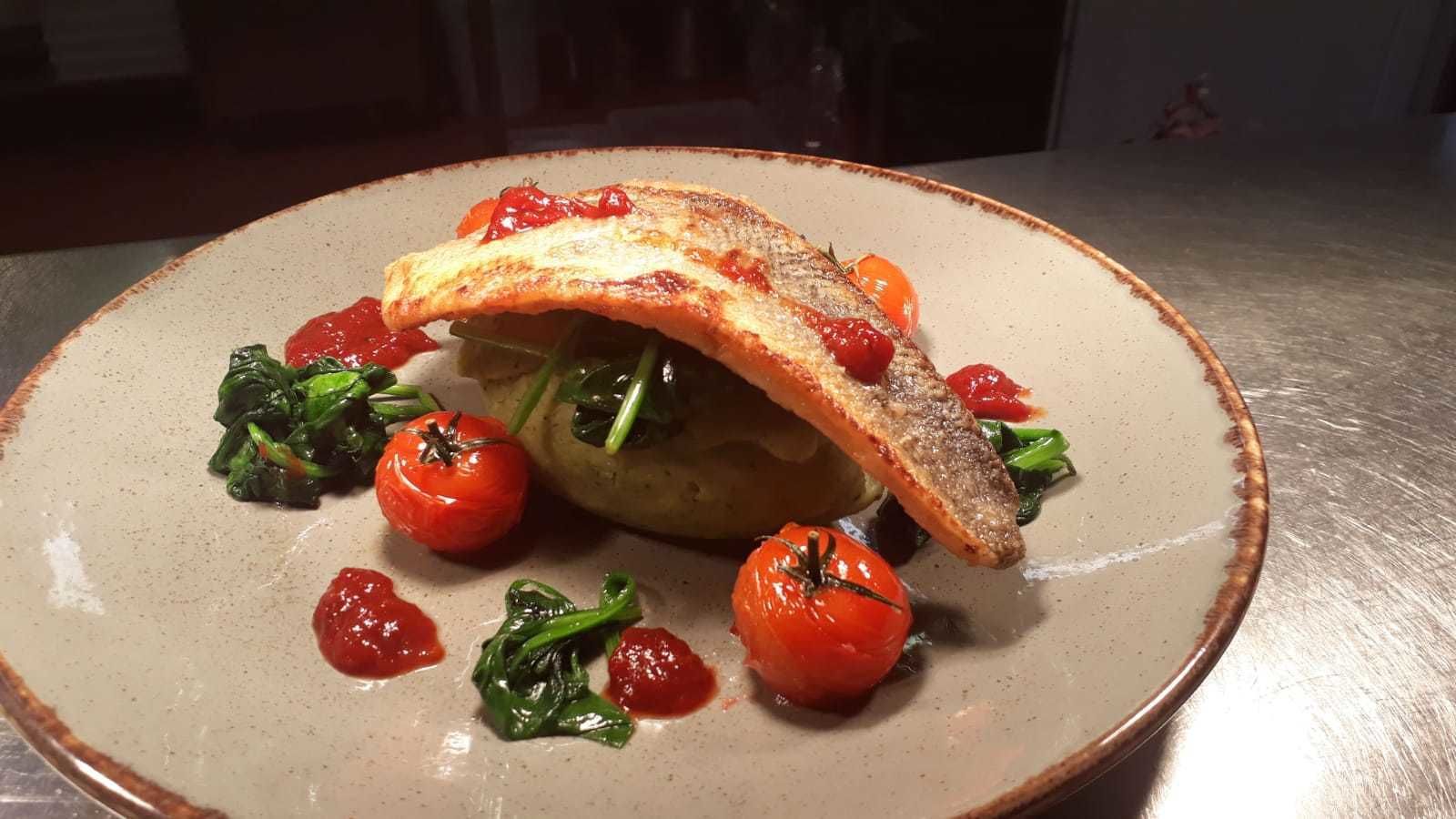 A plate with a fish fillet, cherry tomatoes, and greens.