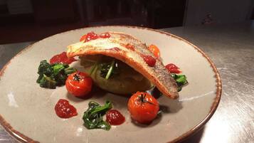 A plate with a fish fillet, cherry tomatoes, and greens.