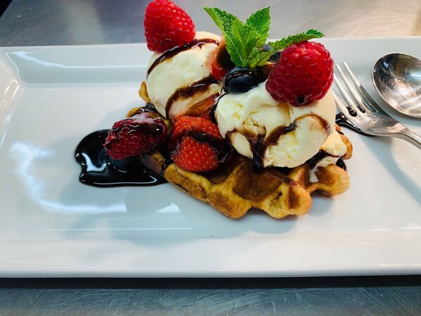 A plate with waffles topped with ice cream, berries, and chocolate sauce. - The Avenue Hotel (Blackburn)