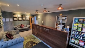 A reception area with a wooden reception desk, two sofas, framed pictures on the wall, a clock, and a vending machine.