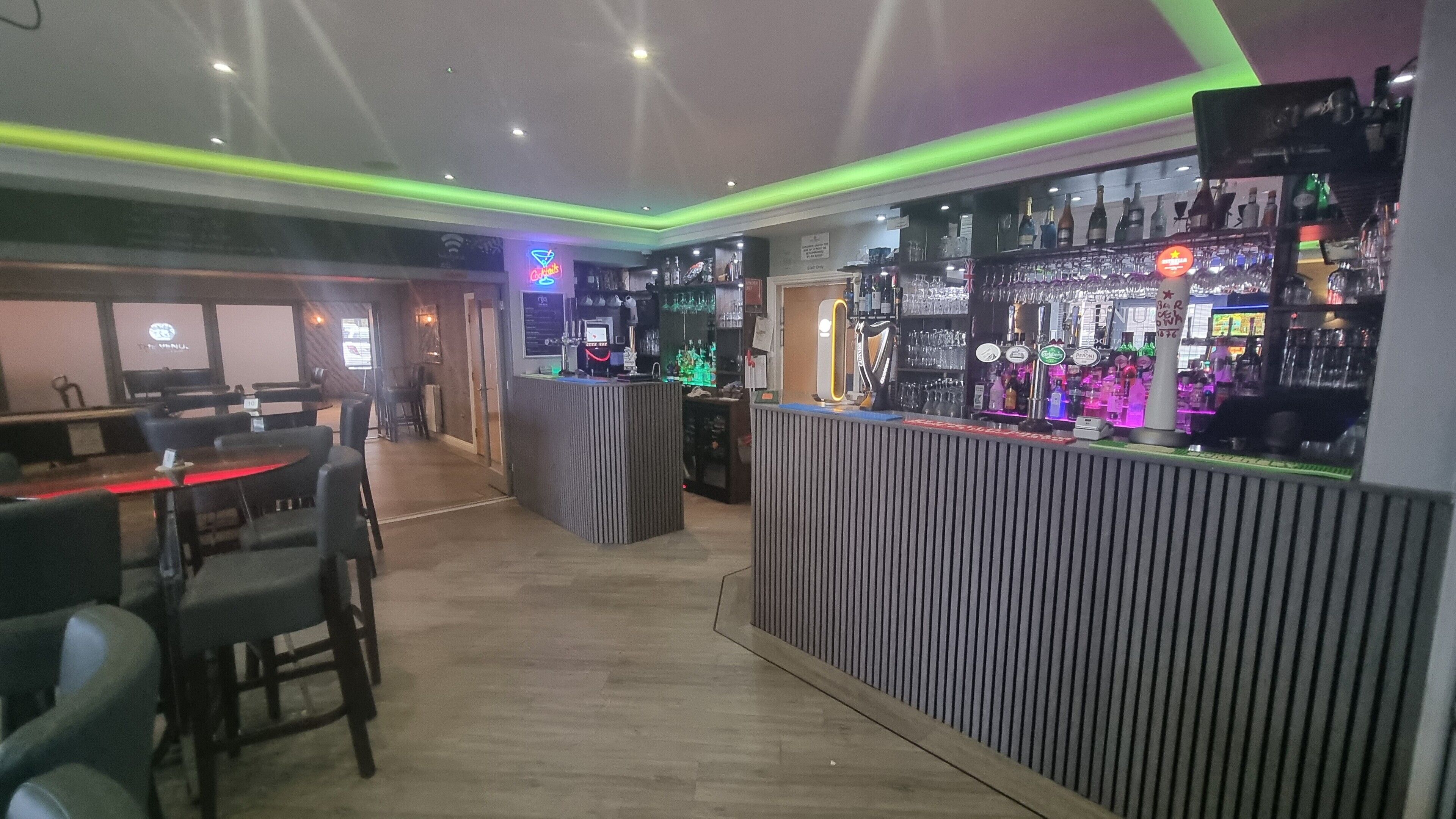 Zona de bar con suelo de madera, una barra con varias botellas y un área de estar con mesas y sillas.