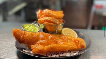 A plate of fried fish with lemon wedges and green sauce.