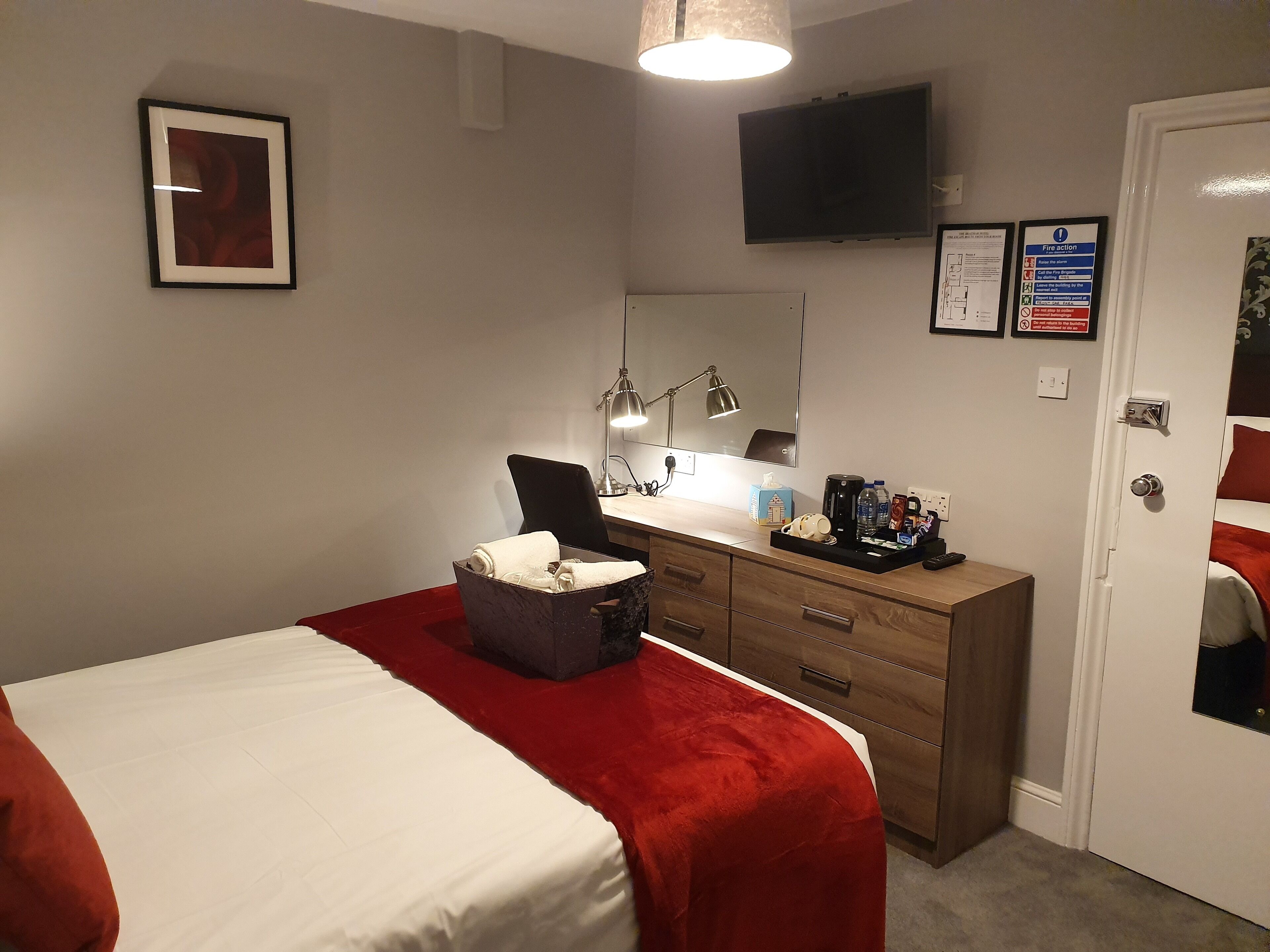 Une chambre d’hôtel avec un lit, un bureau doté d’une lampe, une machine à café et un téléviseur fixé au mur.