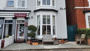 A corner house with a bay window, a front door, and a small outdoor seating area with a bench and chairs. - The Braemar Southport (Southport)