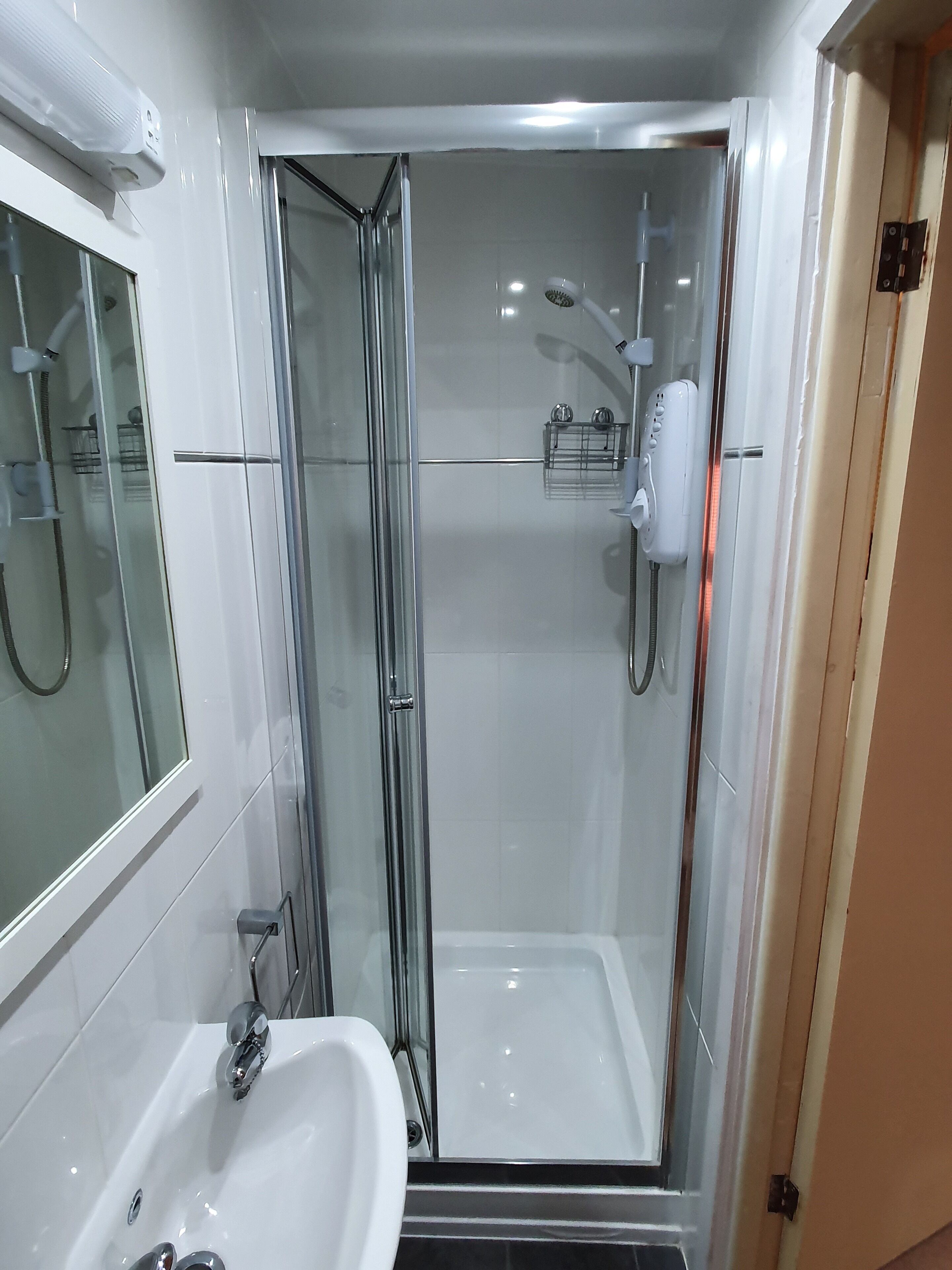 A modern bathroom with a glass-enclosed shower, a white sink, and a handheld showerhead.