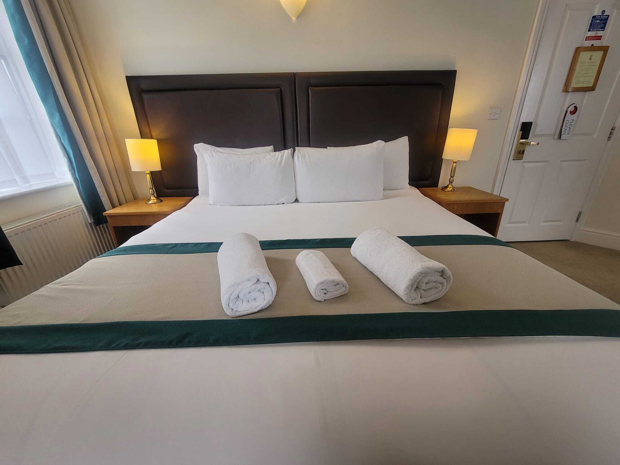 A neatly made bed with white linens, two rolled towels, and a dark headboard.