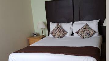 A neatly made bed with a dark headboard, white bedding, and patterned pillows.