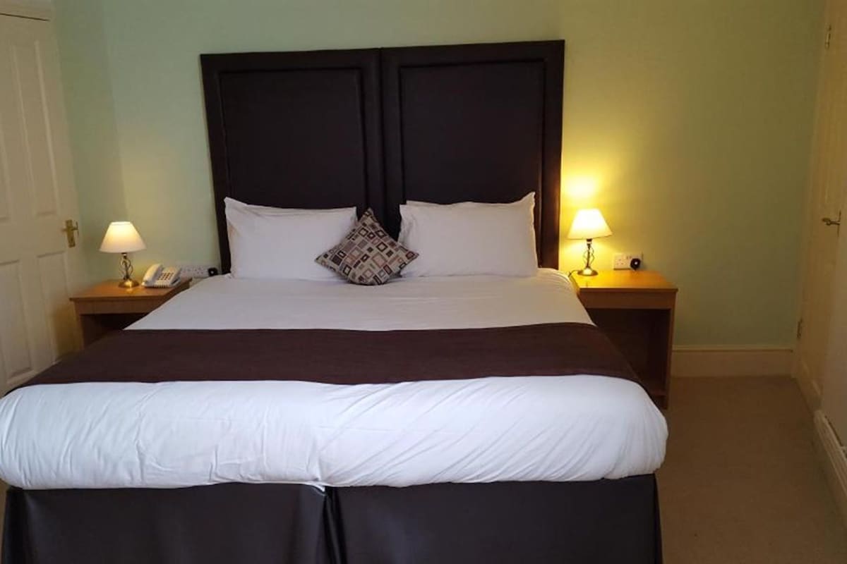 A hotel room with a large bed, two bedside tables with lamps, and a door.