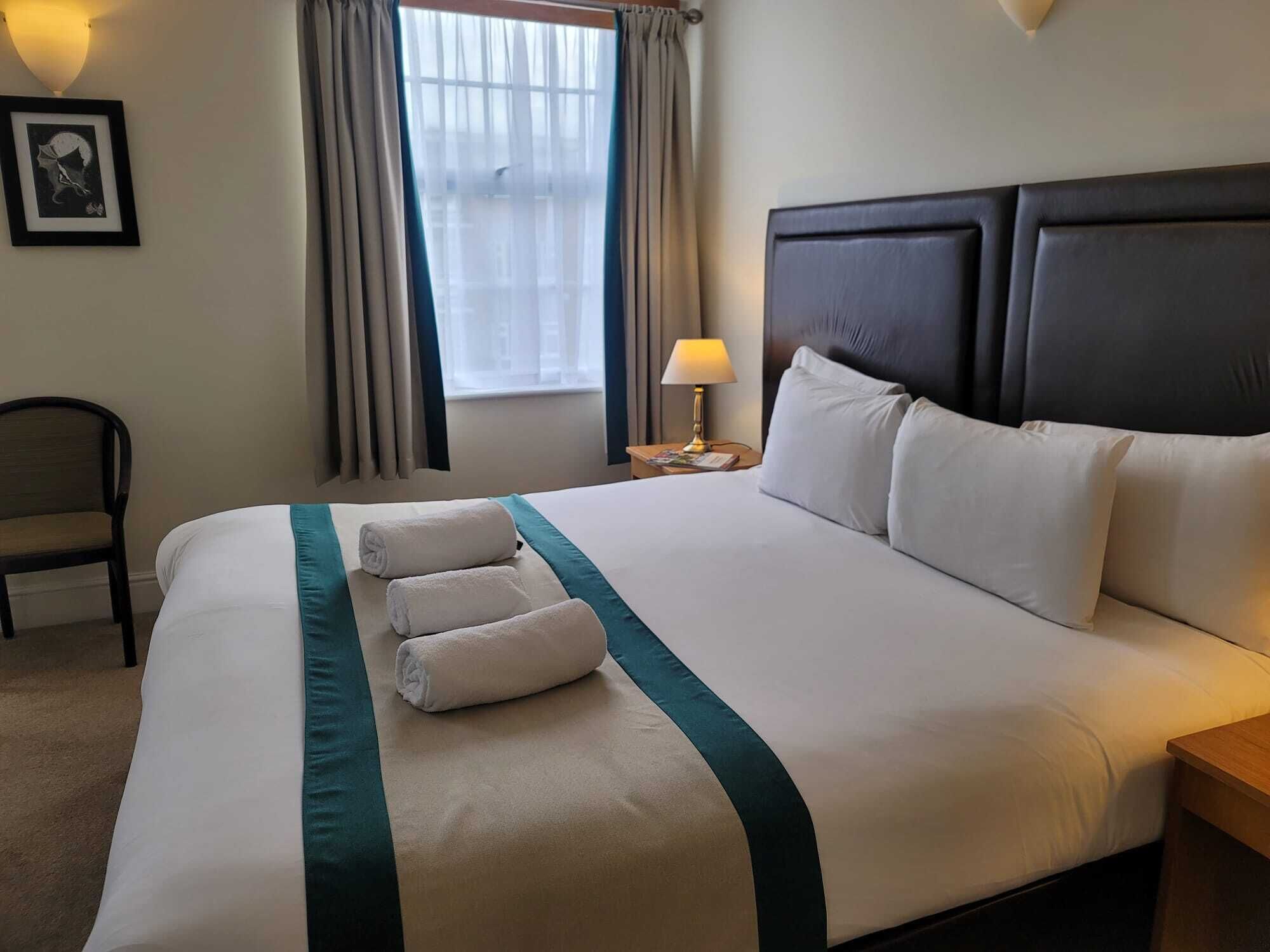 Een net opgemaakt bed met witte lakens en teal accenten, een bedlampje en een ingelijst beeld aan de muur.