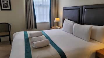 Een net opgemaakt bed met witte lakens en teal accenten, een bedlampje en een ingelijst beeld aan de muur.