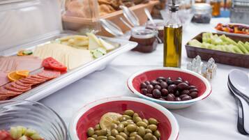 Buffet com diversos alimentos, incluindo carnes, queijos, azeitonas e frutas.