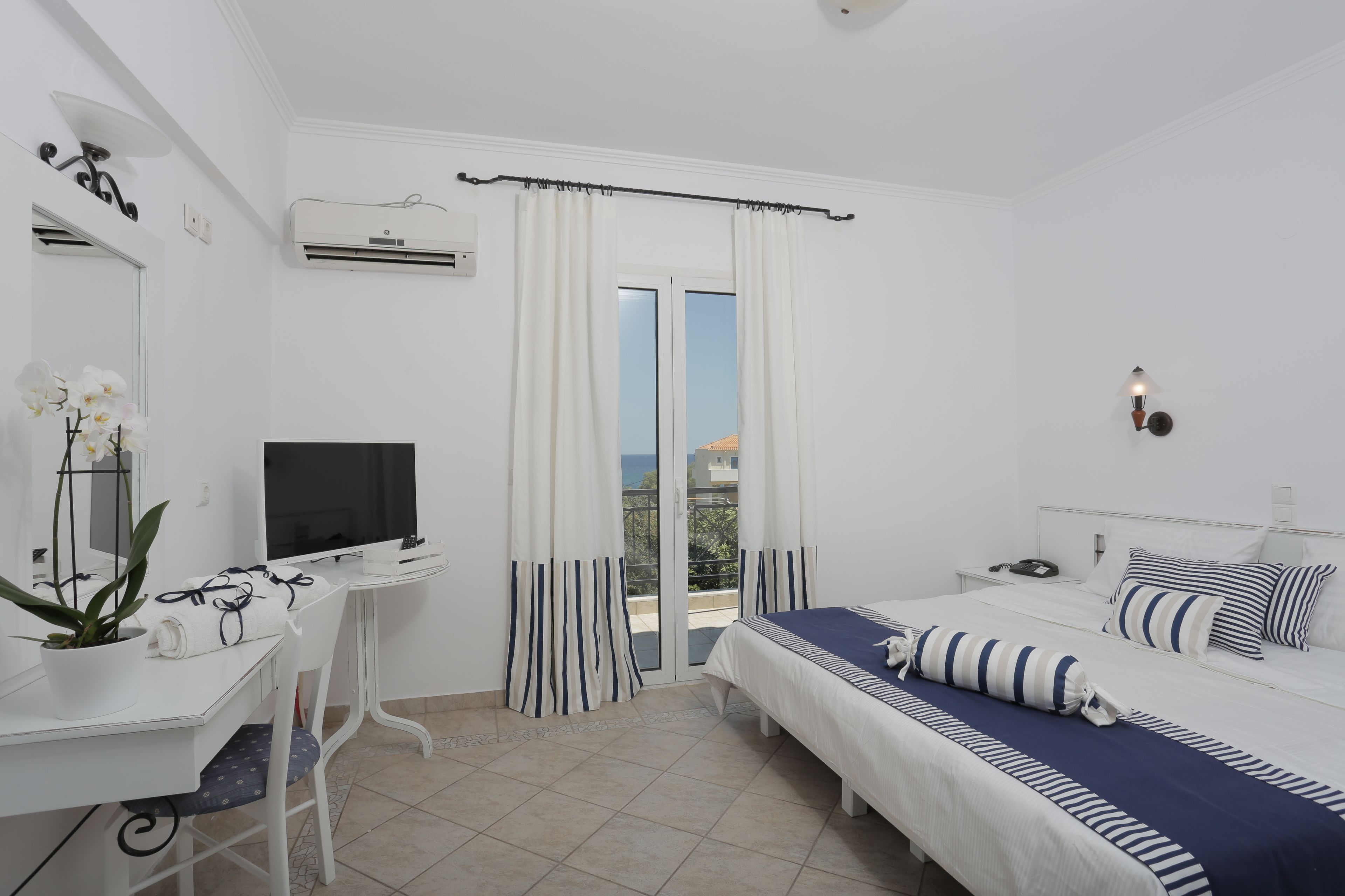 A hotel room with a bed, a desk, a TV, and a balcony with curtains.