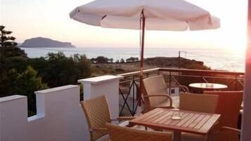 An outdoor seating area with a table and chairs, an umbrella, and a view of the sea and a distant island.