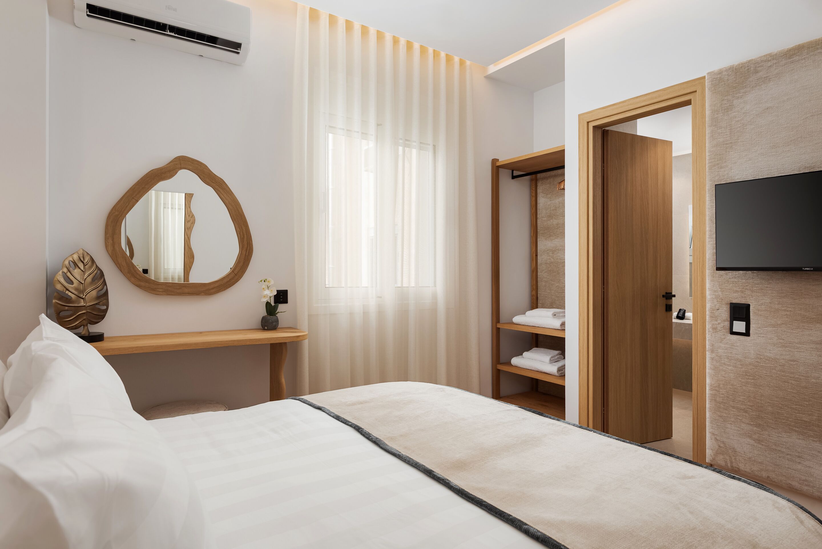 Quarto de hotel com cama, mesa de cabeceira, espelho, guarda-roupa e televisão.