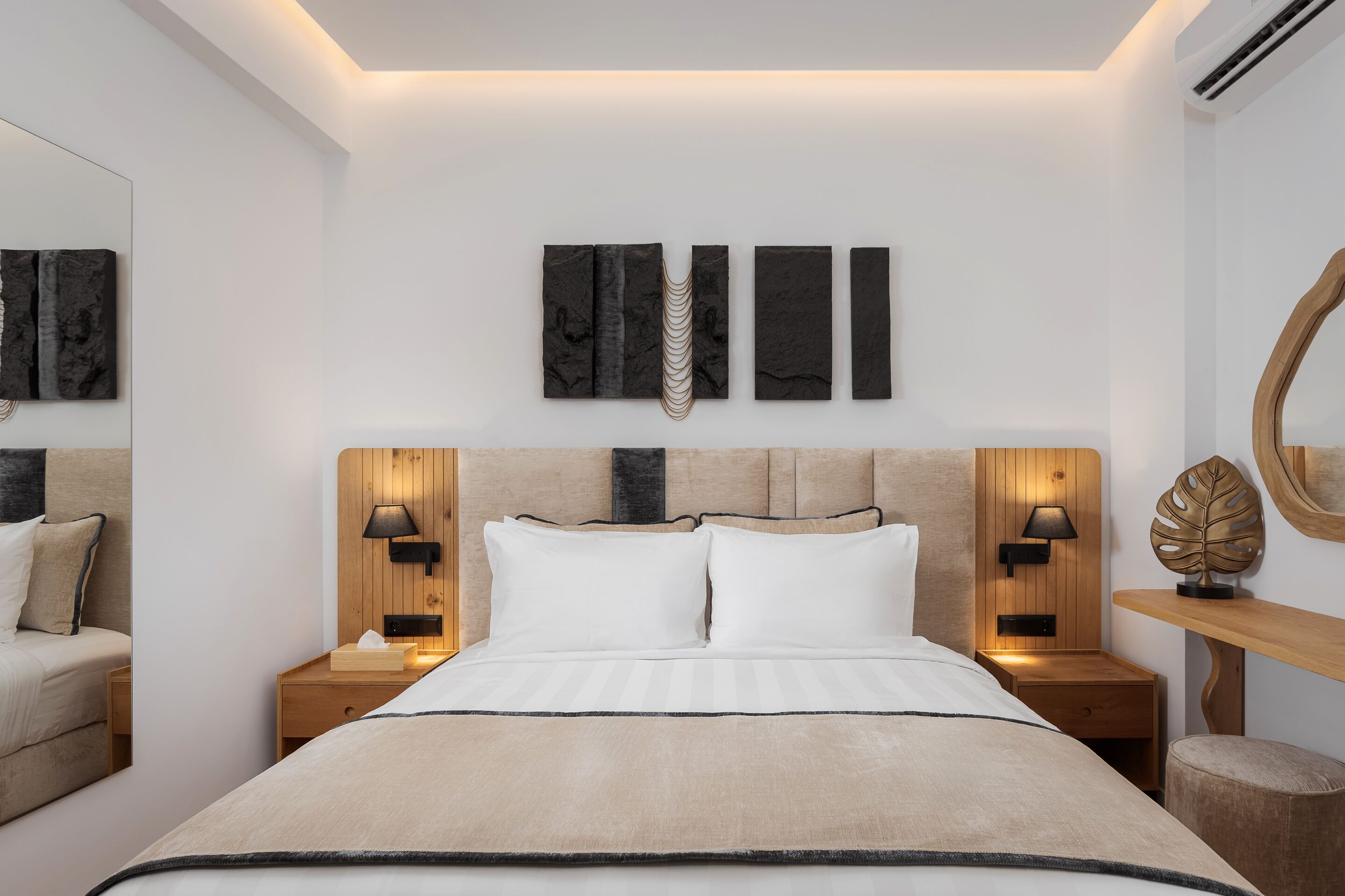 A modern bedroom with a large bed, two bedside tables with lamps, a wooden headboard, and a wall-mounted mirror.