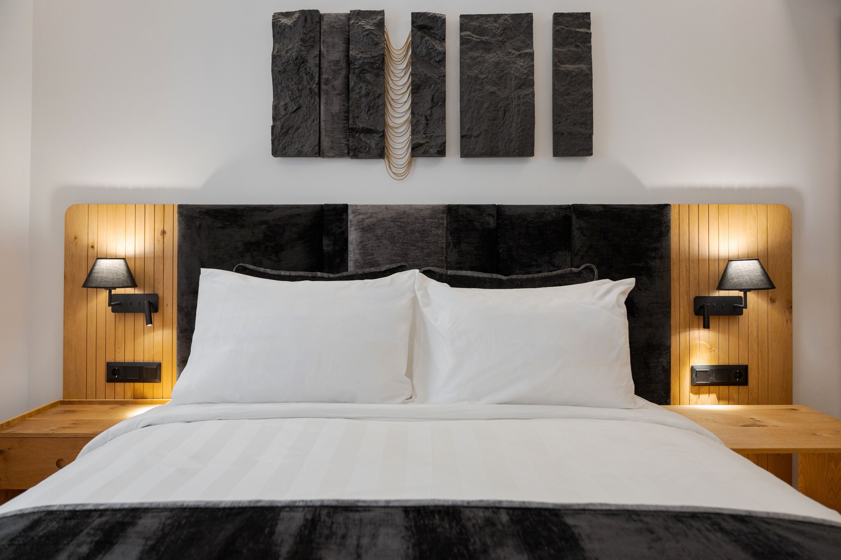 Une chambre à coucher moderne avec une tête de lit noire en tissu, une literie blanche et deux lampes de chevet.