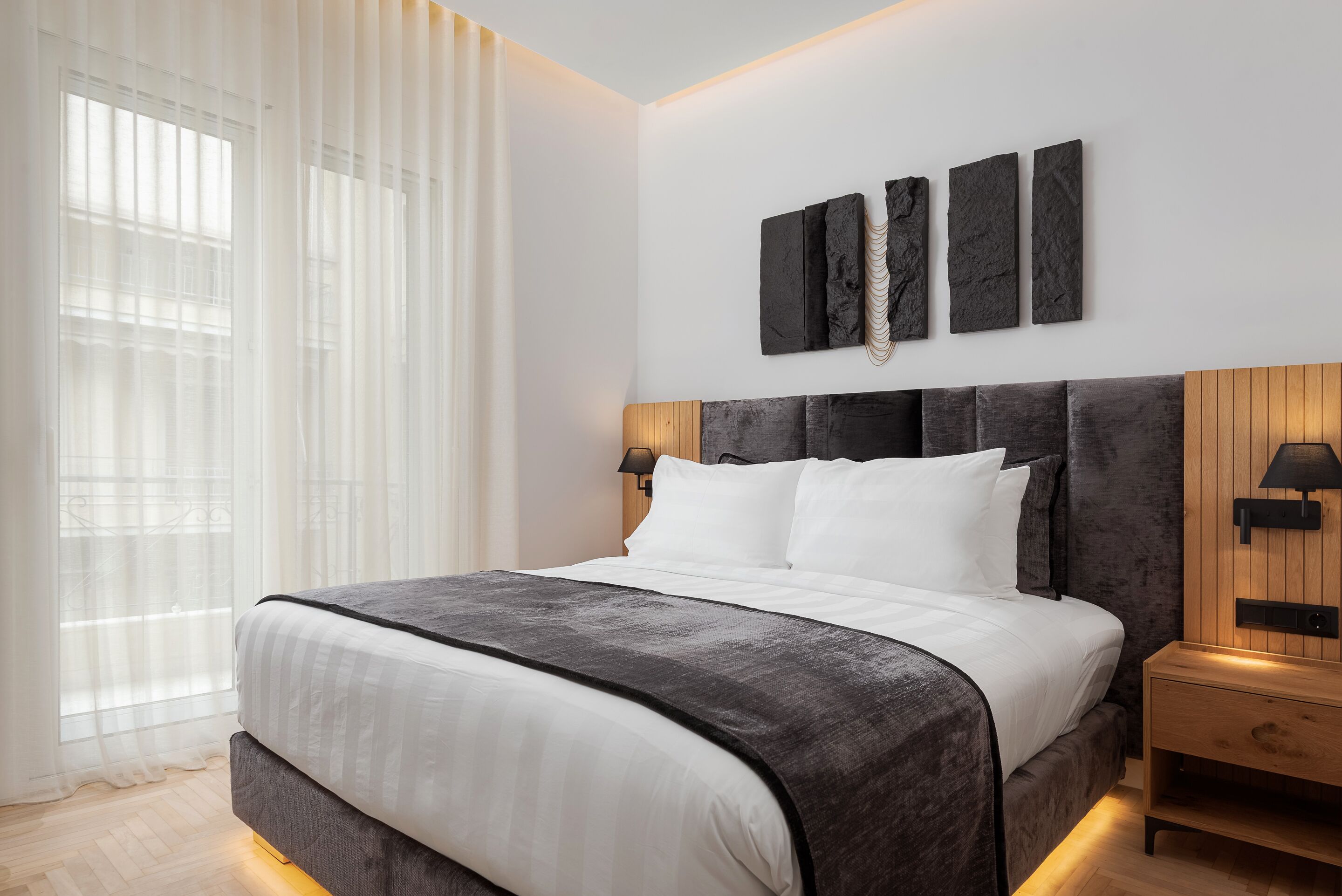 A modern bedroom with a large bed, a wooden headboard, and a nightstand with a lamp.