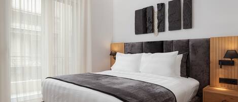 A modern bedroom with a large bed, a wooden headboard, and a nightstand with a lamp.