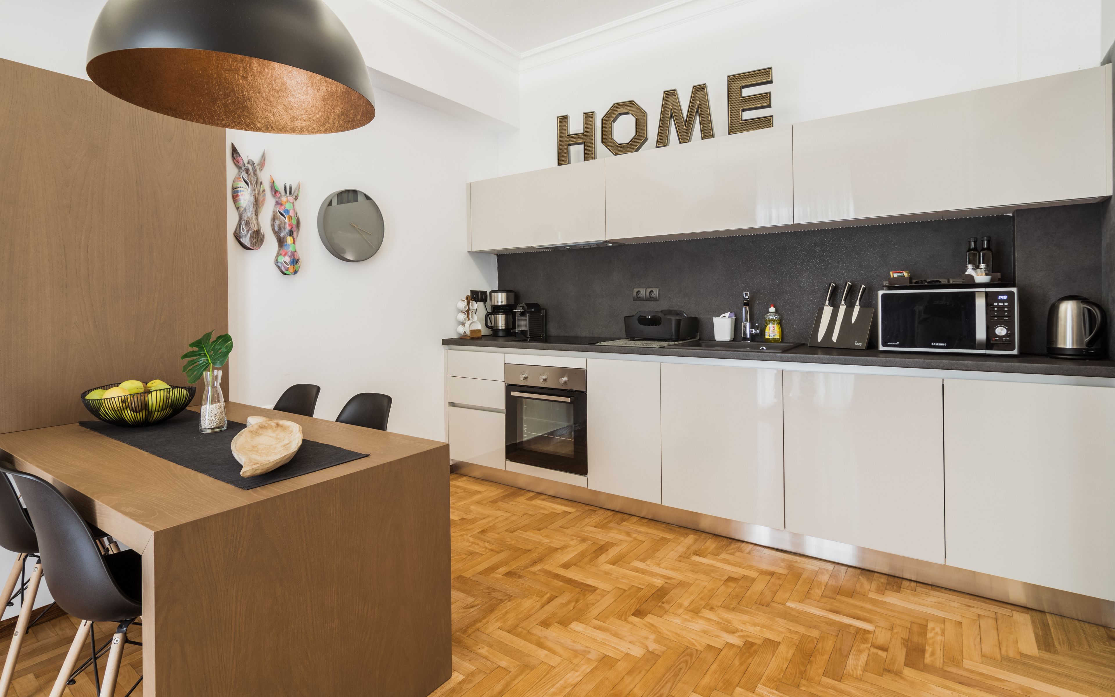 A modern kitchen with white cabinets, a black countertop, and a wooden dining table.