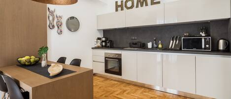 A modern kitchen with white cabinets, a black countertop, and a wooden dining table.