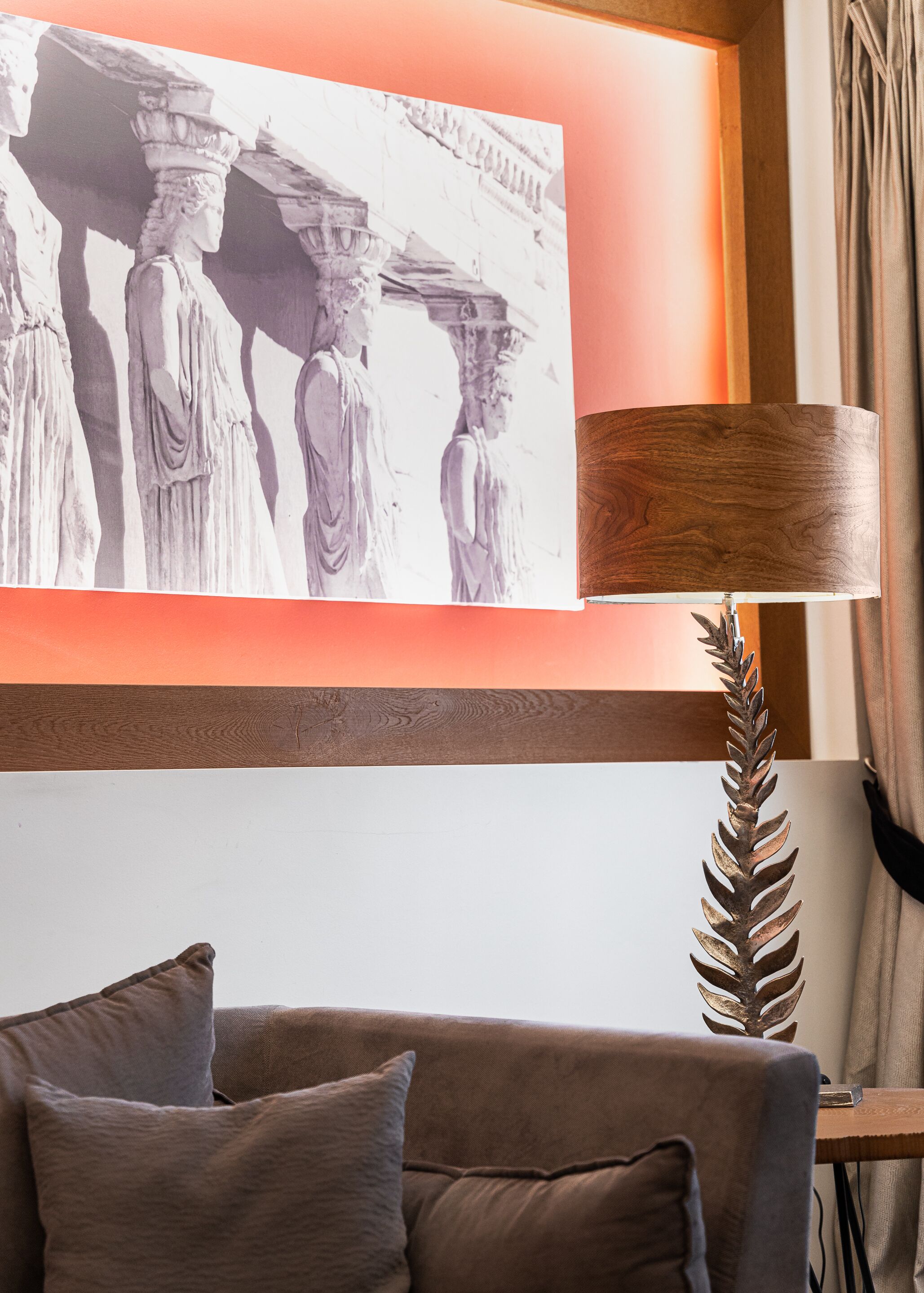 Uma sala de estar moderna com uma grande obra de arte emoldurada retratando figuras clássicas, uma mesa lateral de madeira com uma peça de metal decorativa e um sofá marrom com almofadas.