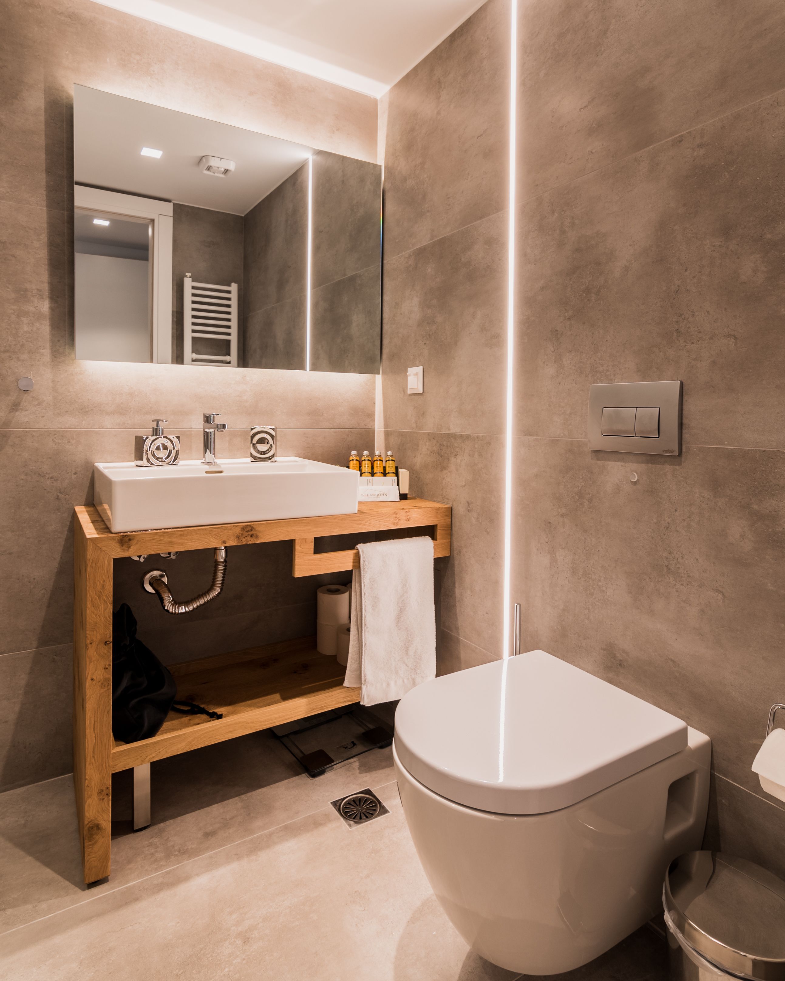 A modern bathroom with a wooden vanity, a large mirror, a white toilet, and a towel hanging on the wall.