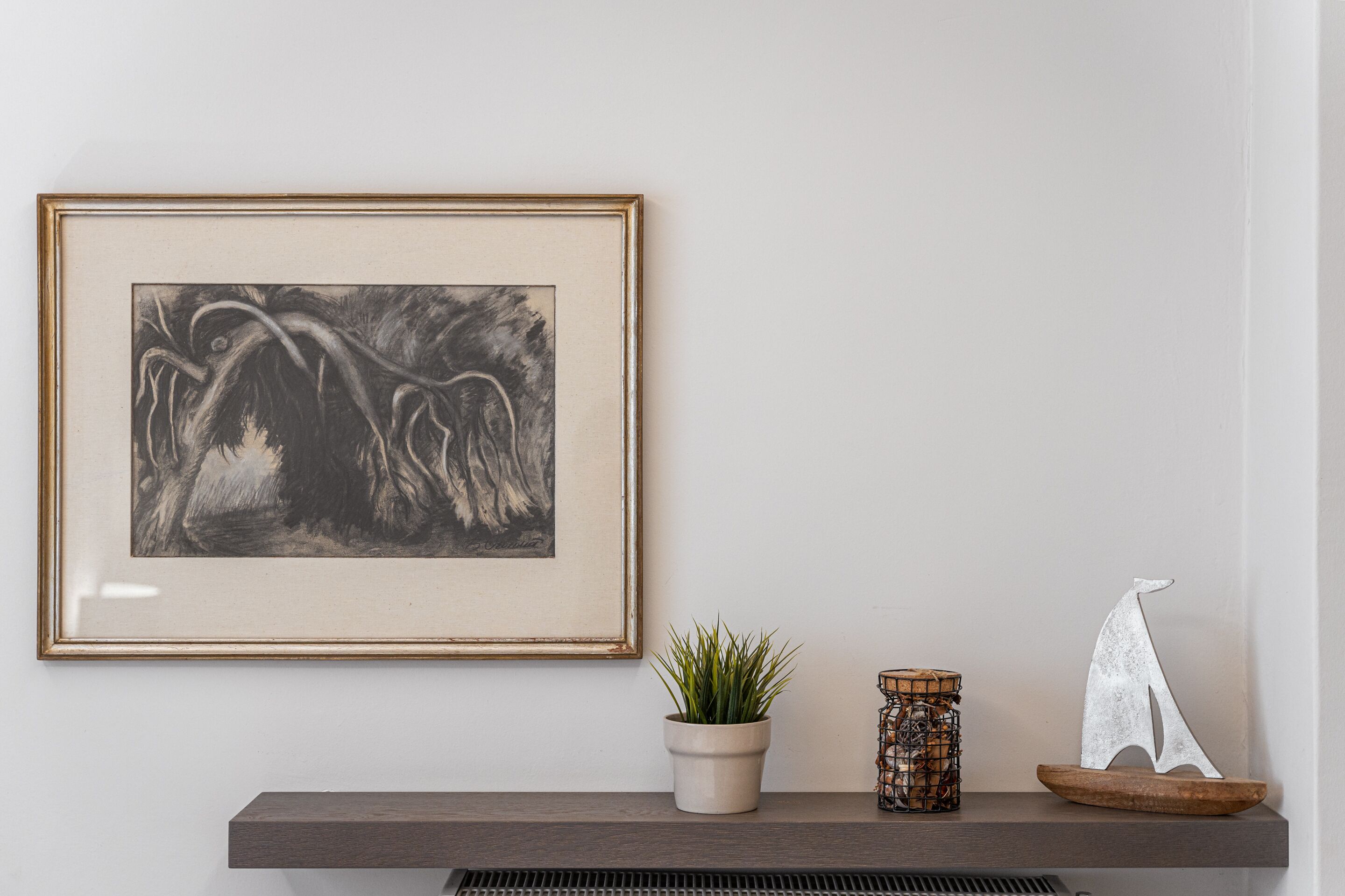 A framed artwork, a potted plant, and a decorative sailboat on a shelf.