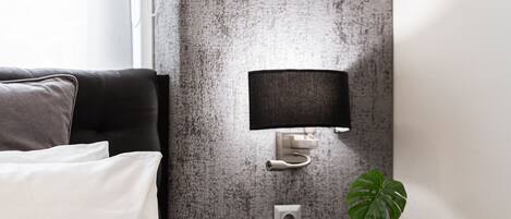 A modern hotel room with a bed, a nightstand with a lamp, and a small plant.