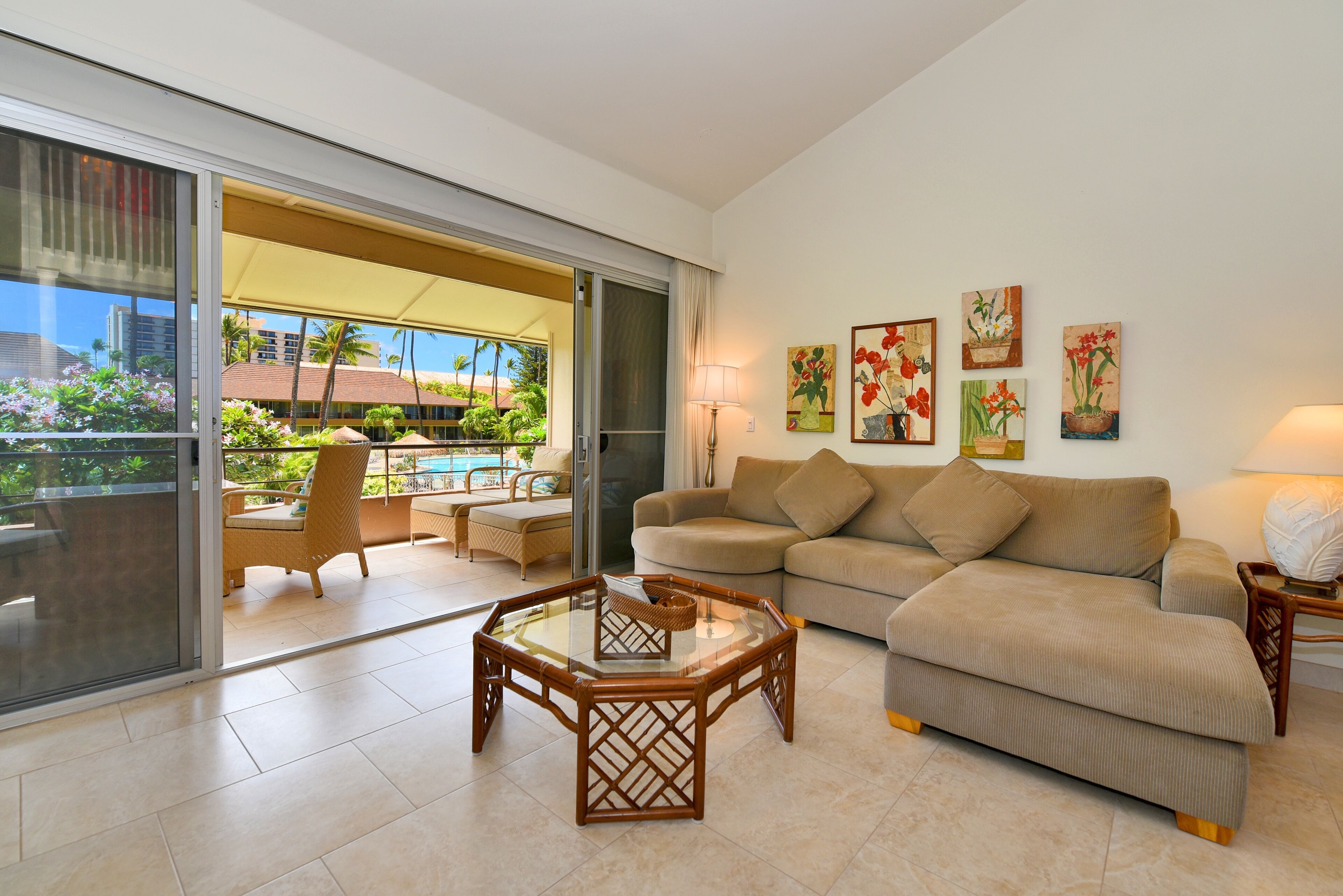 A living room with a glass door leading to a balcony, a beige sofa, a glass coffee table, and a wicker chair.