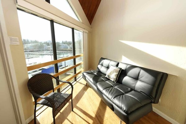 A room with a black leather sofa, a wicker chair, and large windows offering a view of a marina. - 497 Tahoe Keys Blvd, 34a 2 Bedroom Condo by RedAwning (South Lake Tahoe)