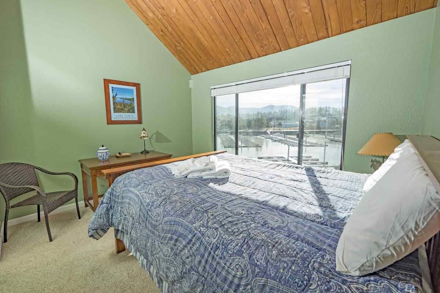 Una camera da letto con un letto, una scrivania e una sedia. Si vede una finestra con vista su un lago e montagne.