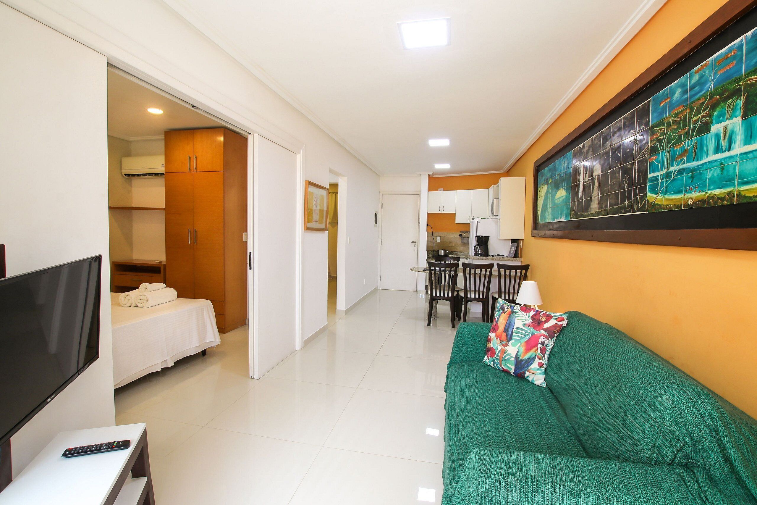 Habitación de hotel con cama, televisor, sofá verde y zona de comedor con sillas y mesa.