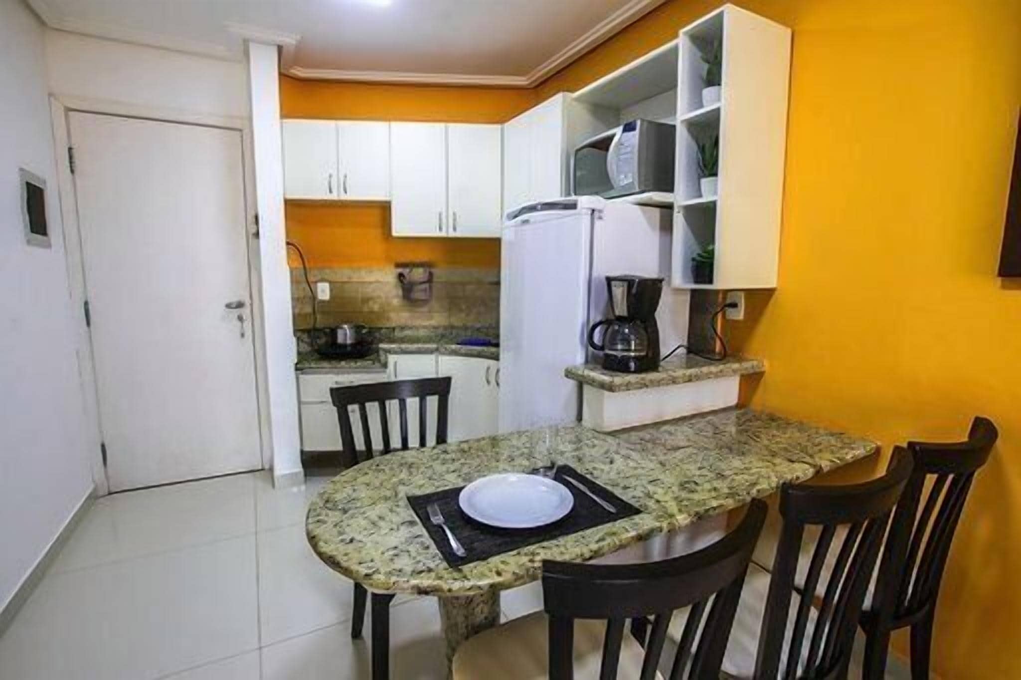 Cocina compacta con gabinetes blancos, microondas y cafetera.