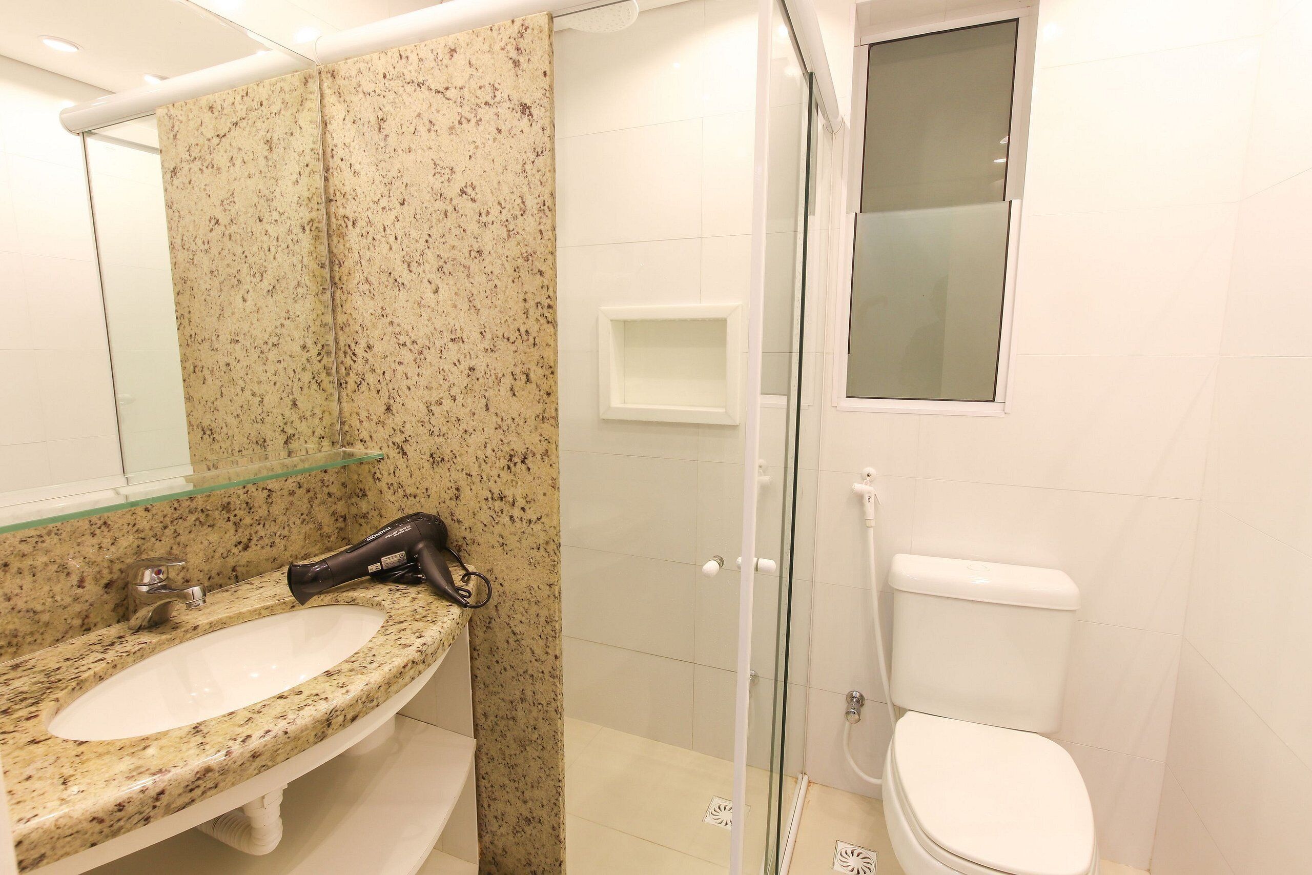 Un baño con lavamanos de granito, cabina de ducha con mampara de vidrio y retrete blanco.