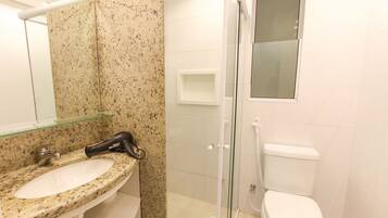 Un baño con lavamanos de granito, cabina de ducha con mampara de vidrio y retrete blanco.