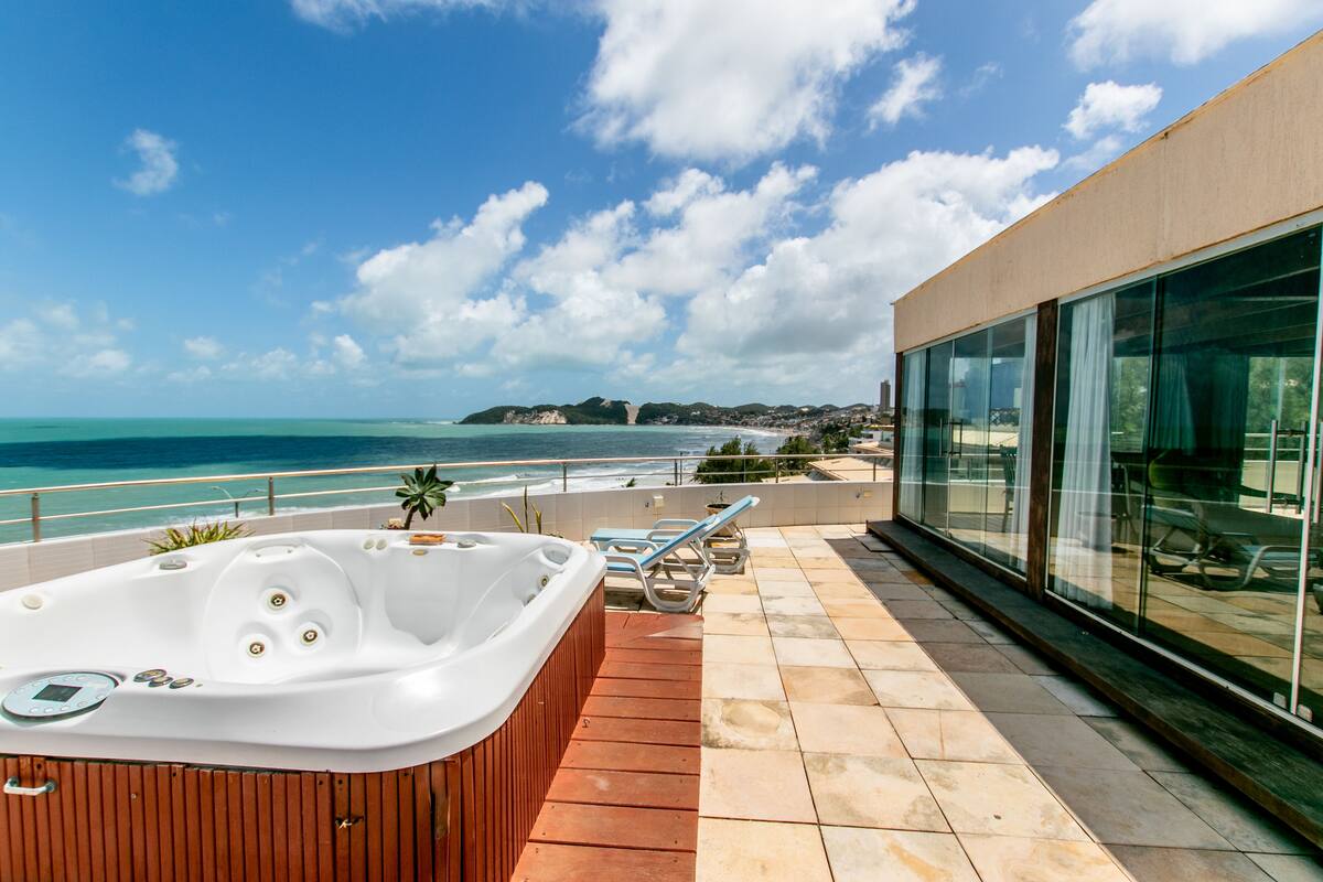 A rooftop terrace with a hot tub, lounge chairs, and a view of the ocean.